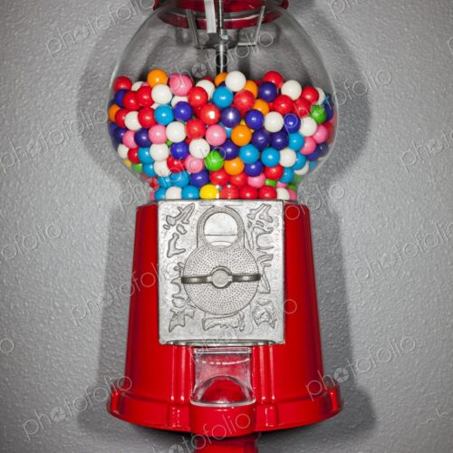 Close-up of a red gumball machine filled with vibrant multicolored gumballs against a…