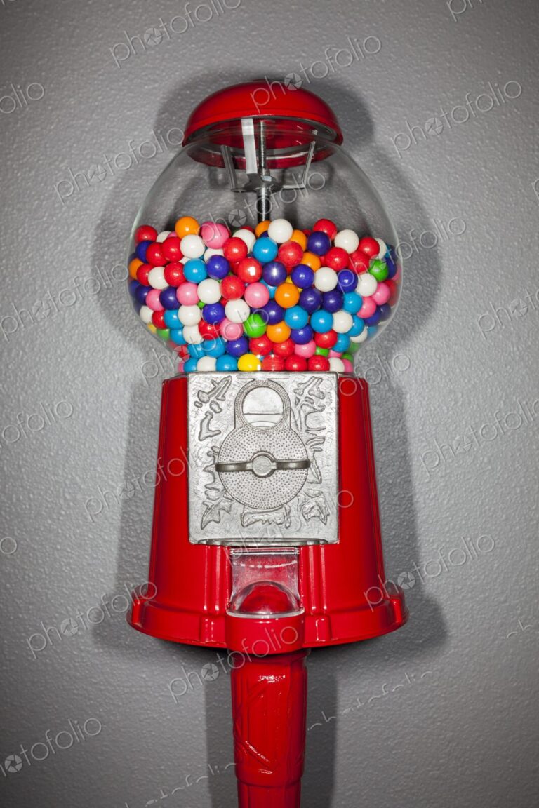 Close-up of a red gumball machine filled with vibrant multicolored gumballs against a…