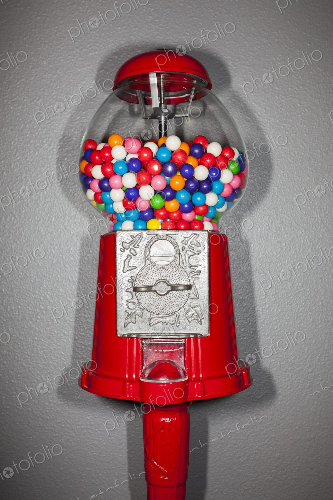Close-up of a red gumball machine filled with vibrant multicolored gumballs against a…