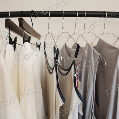 Close up of a selection of clothes in natural colours on a rail in a boutique.