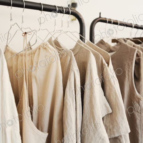 Close up of a selection of clothes in natural colours on a rail in a boutique.