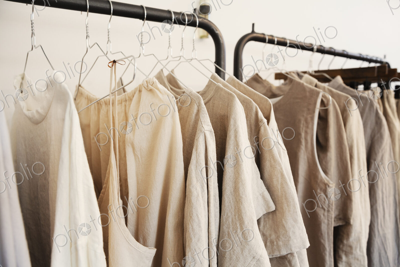 Close up of a selection of clothes in natural colours on a rail in a boutique.