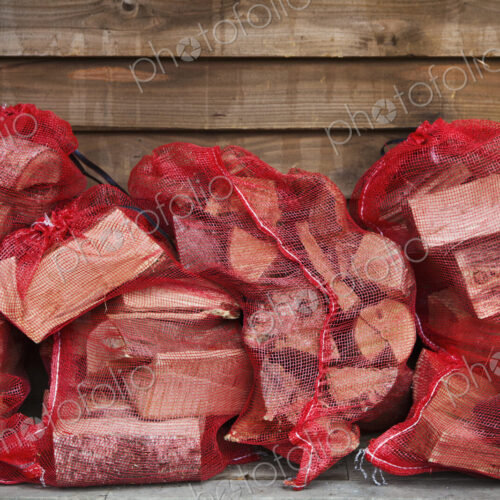 Close up of a stack of firewood in red net bags outside a farm shop. Close up of a stack of firewood in red net bags outside a farm shop.