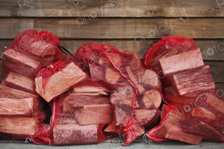 Close up of a stack of firewood in red net bags outside a farm shop.