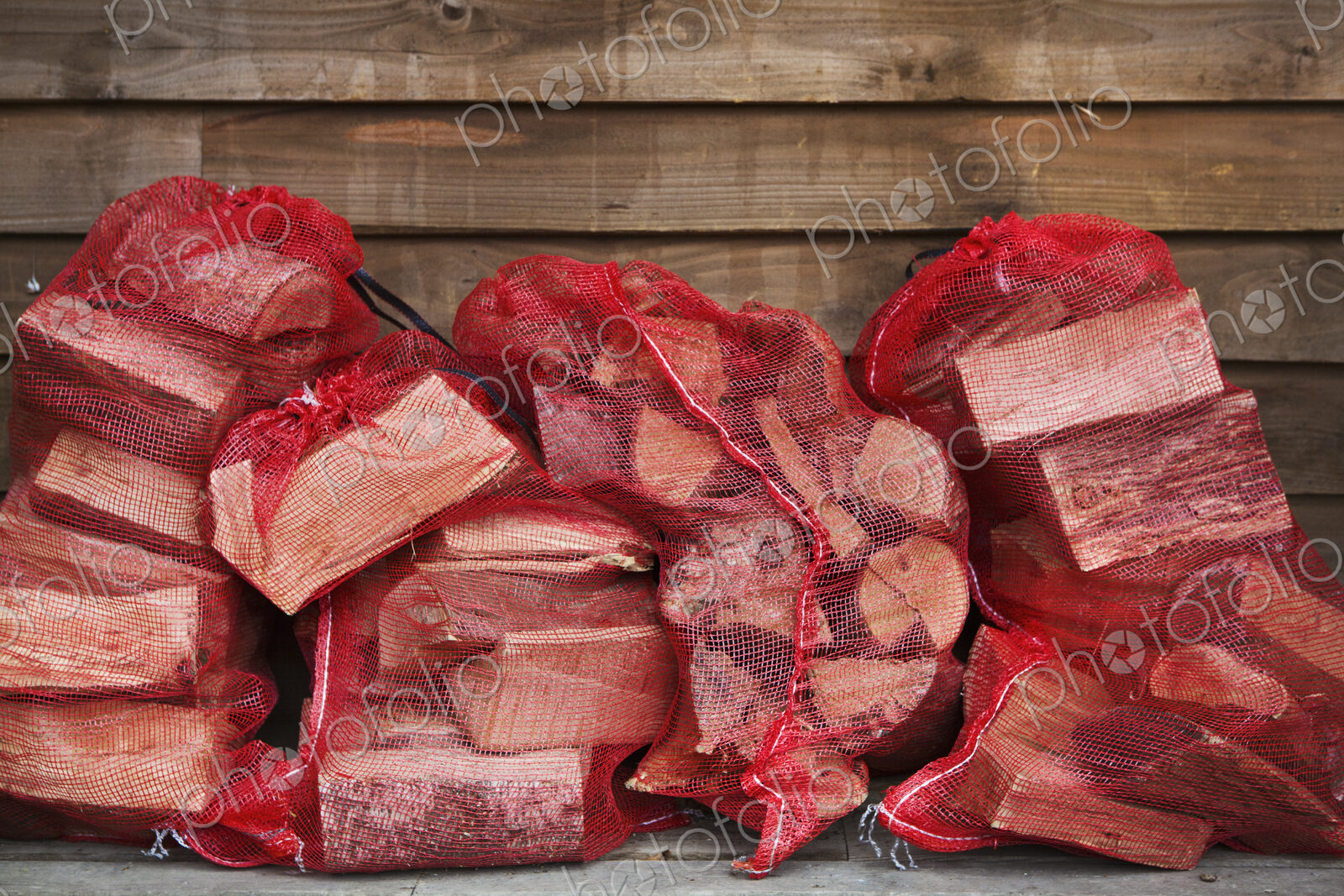 Close up of a stack of firewood in red net bags outside a farm shop.