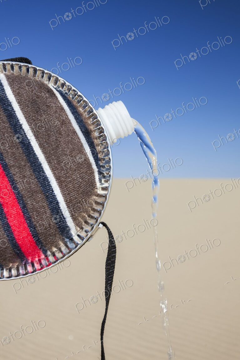 Close-up of a striped fabric-covered canteen tilted to pour out a stream of water,…