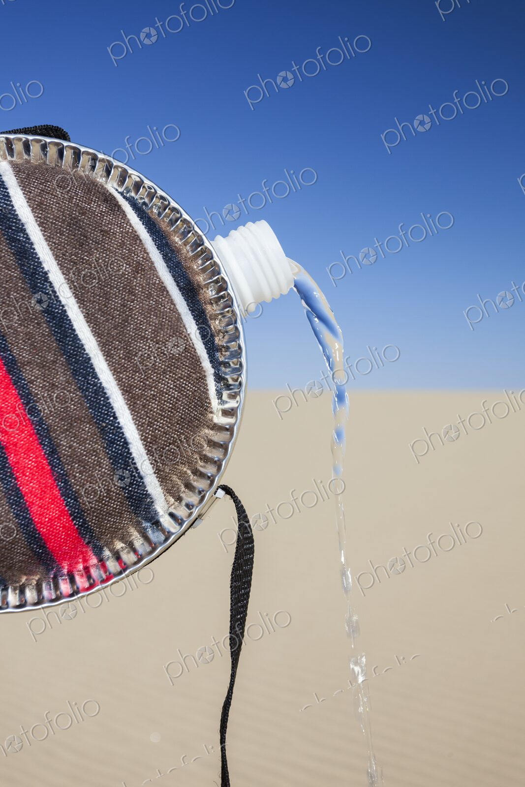 Close-up of a striped fabric-covered canteen tilted to pour out a stream of water,…