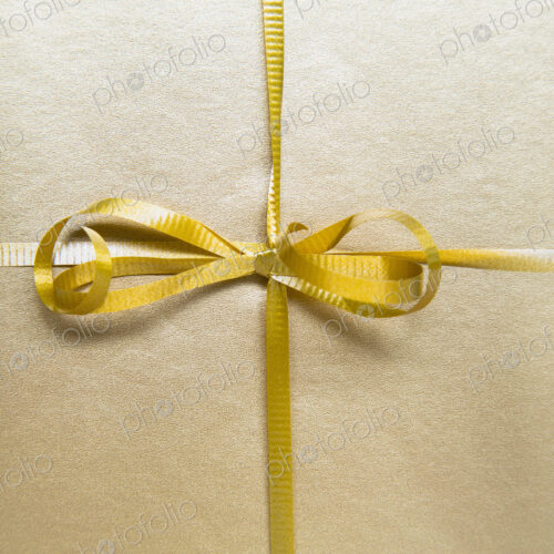 Close up of a tied bow and gold ribbon from a wrapped gift. Close up of a tied bow and gold ribbon from a wrapped gift.