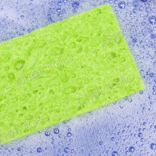Close-up of a vibrant green sponge resting in a bowl of foamy soapy water. The image…