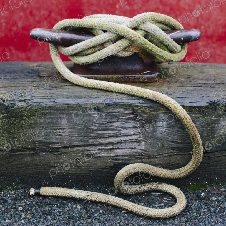 Close up of a wharfside mooring cleat with a fishing boat rope tied around it.