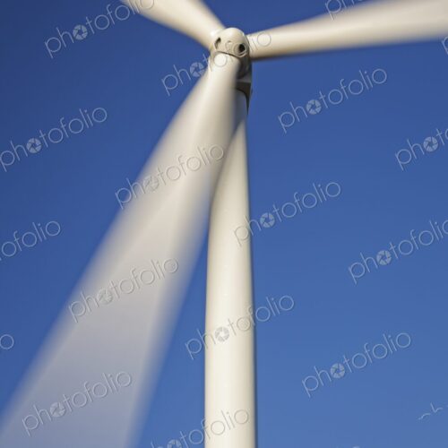 Close-up of a wind turbine with spinning blades against a clear blue sky, symbolizing… Close-up of a wind turbine with spinning blades against a clear blue sky, symbolizing…
