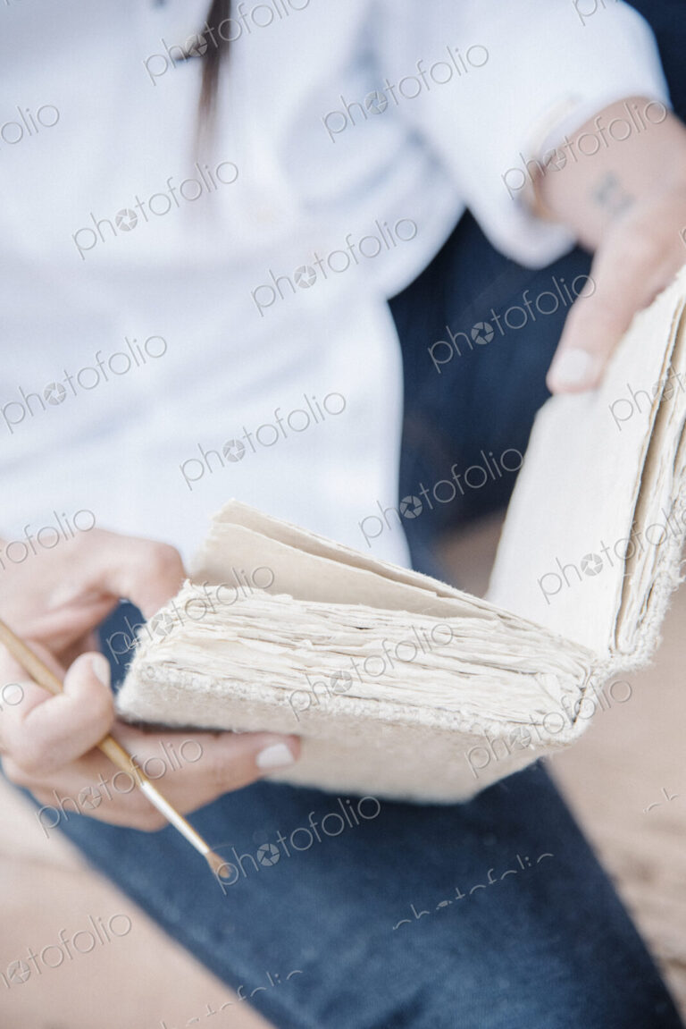 Close up of a woman holding a sketch book and paint brush.