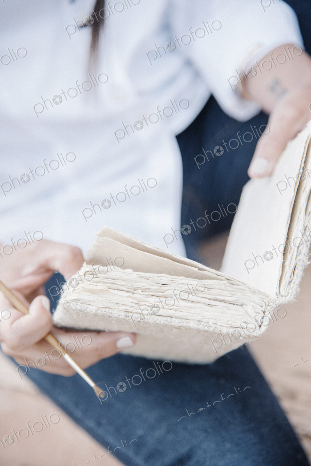 Close up of a woman holding a sketch book and paint brush.