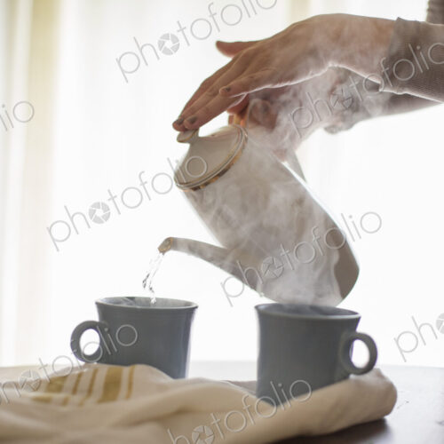 Close up of a woman pouring hot water from a coffee pot into a mug.