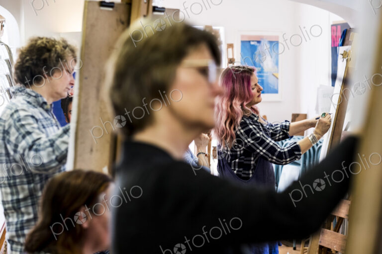 Close up of a woman standing at an easel, drawing.