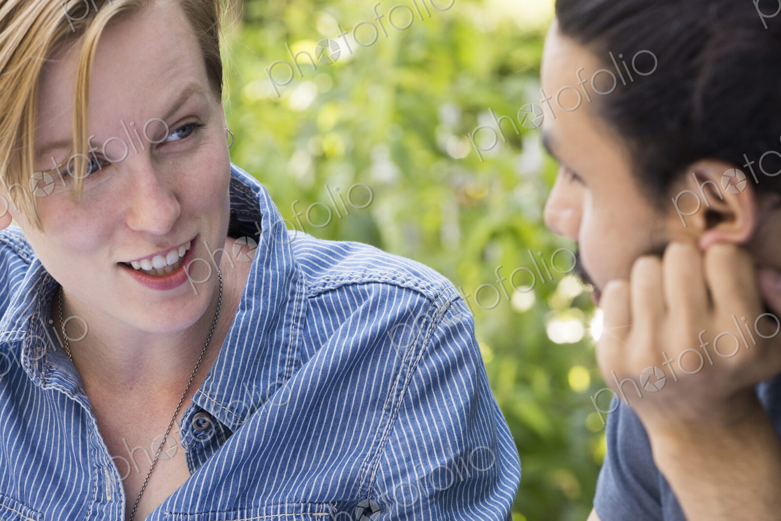 Close up of a young man and woman sitting side by side, smiling and talking.