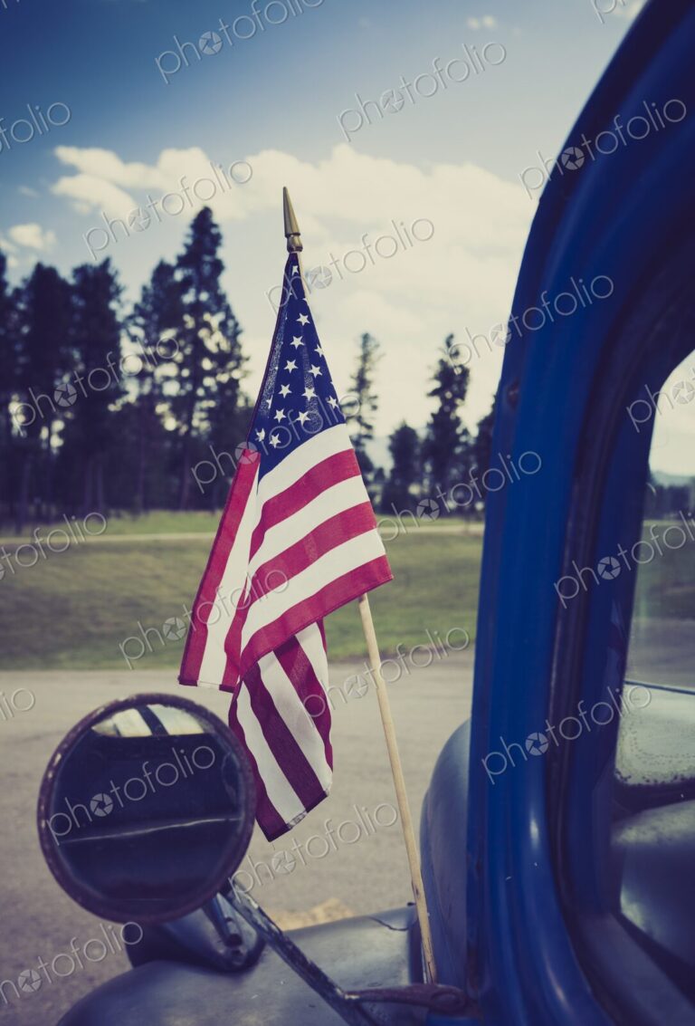 Close-up of an American flag mounted on an antique truck in Hill City, South Dakota,…