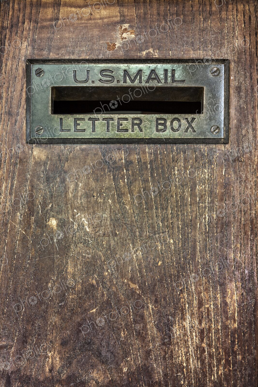 Close up of an antique U.S. Mail letter slot set in a worn wooden door, showing brass…