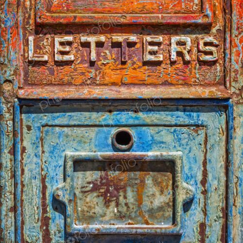 Close up of an antique metal mailbox with peeling turquoise and orange paint and the…