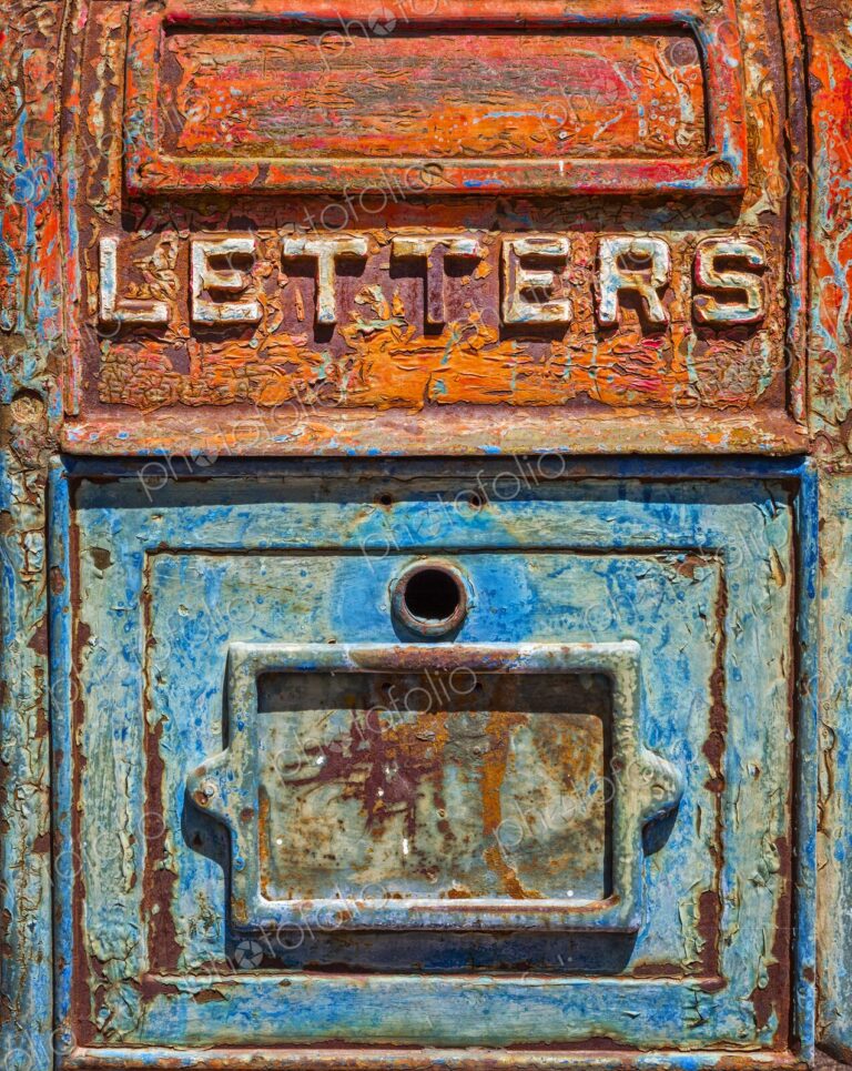 Close up of an antique metal mailbox with peeling turquoise and orange paint and the…