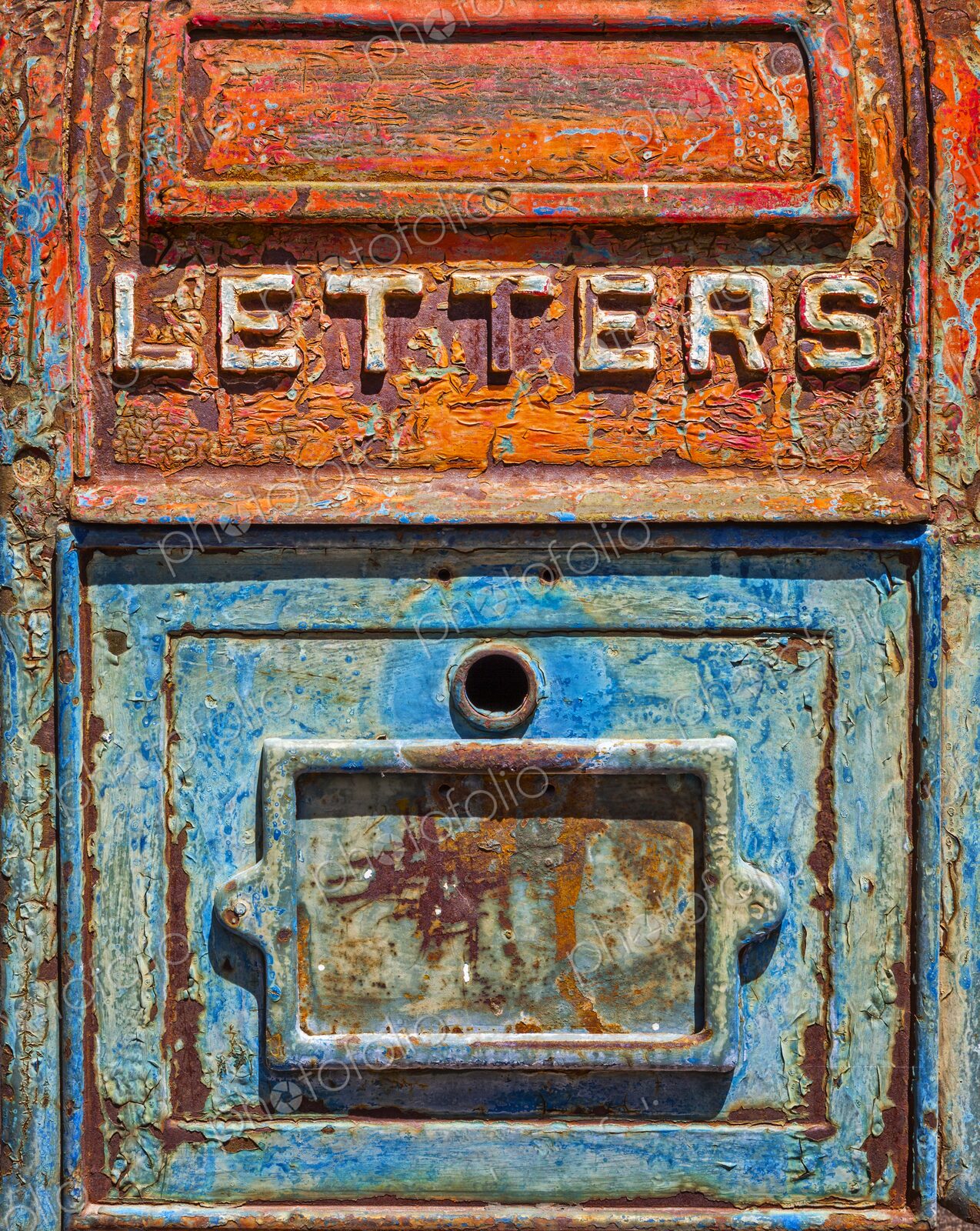 Close up of an antique metal mailbox with peeling turquoise and orange paint and the…