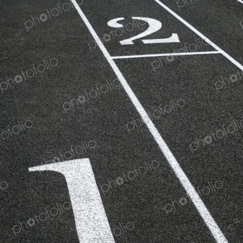 Close-up of black asphalt running track with white lane numbers and dividing lines -…