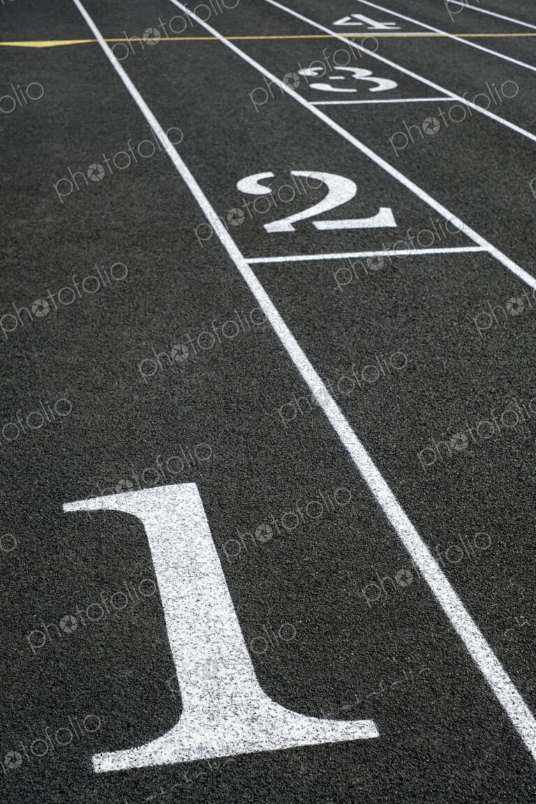 Close-up of black asphalt running track with white lane numbers and dividing lines -…