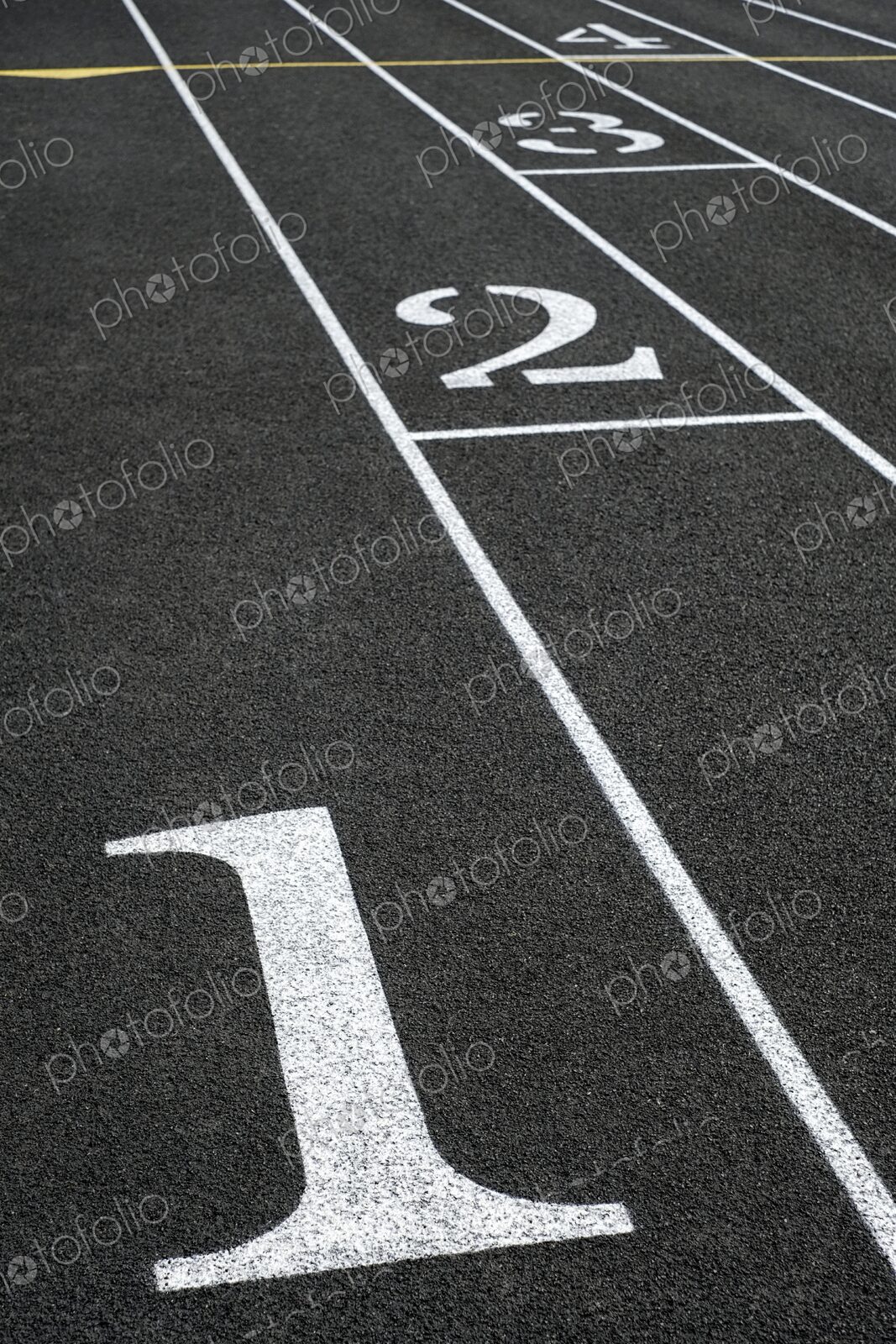 Close-up of black asphalt running track with white lane numbers and dividing lines -…