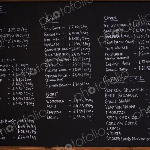 Close up of blackboard with handwritten list of cheese and charcuterie products in a… Close up of blackboard with handwritten list of cheese and charcuterie products in a…