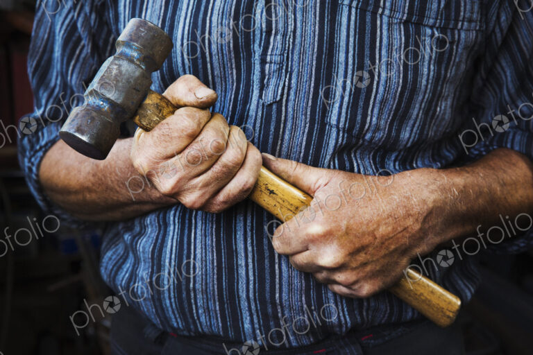 Close up of blacksmith's hands gripping a large hammer.