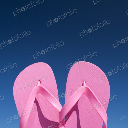 Close-up of bright pink flip flops held up against a vivid blue sky on a sunny day. Close-up of bright pink flip flops held up against a vivid blue sky on a sunny day.