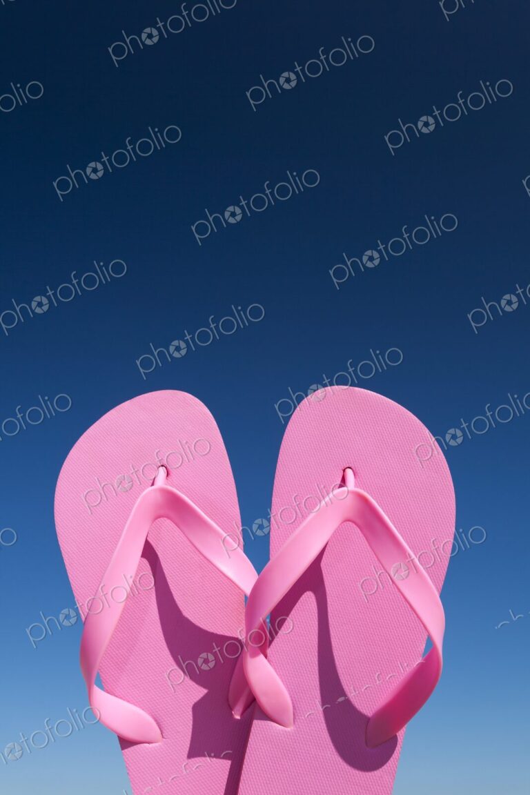 Close-up of bright pink flip flops held up against a vivid blue sky on a sunny day.