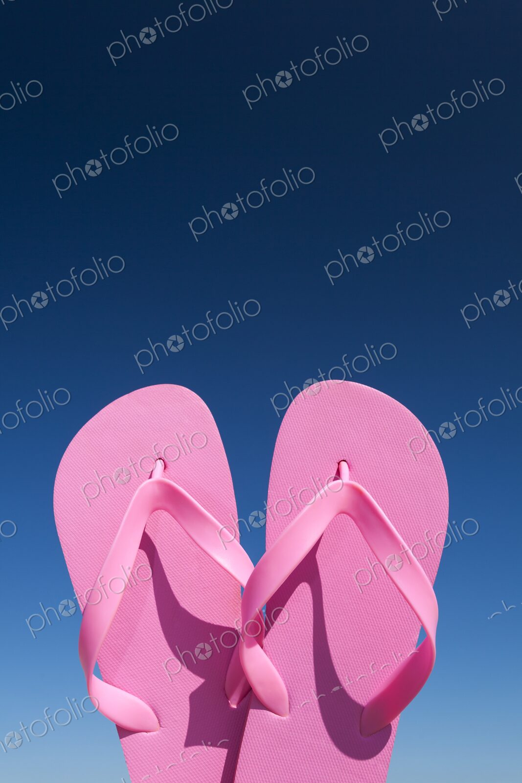 Close-up of bright pink flip flops held up against a vivid blue sky on a sunny day.