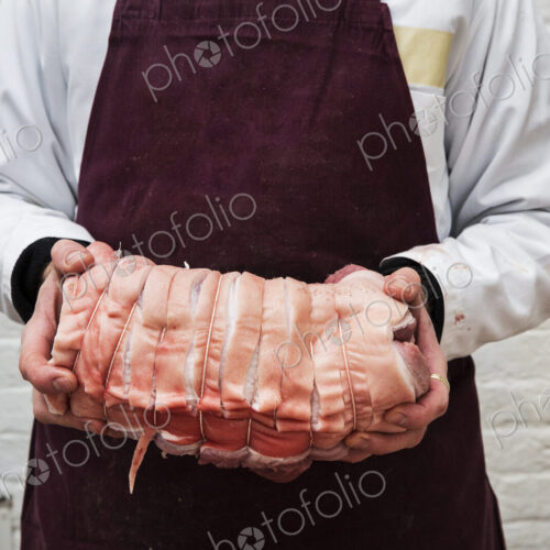 Close up of butcher wearing apron holding large rolled pork belly.