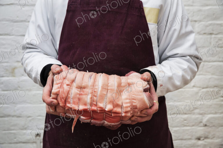 Close up of butcher wearing apron holding large rolled pork belly.