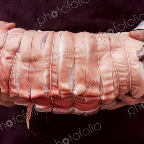 Close up of butcher wearing apron holding large rolled pork belly.