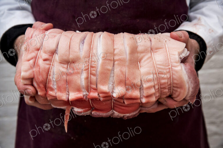 Close up of butcher wearing apron holding large rolled pork belly.