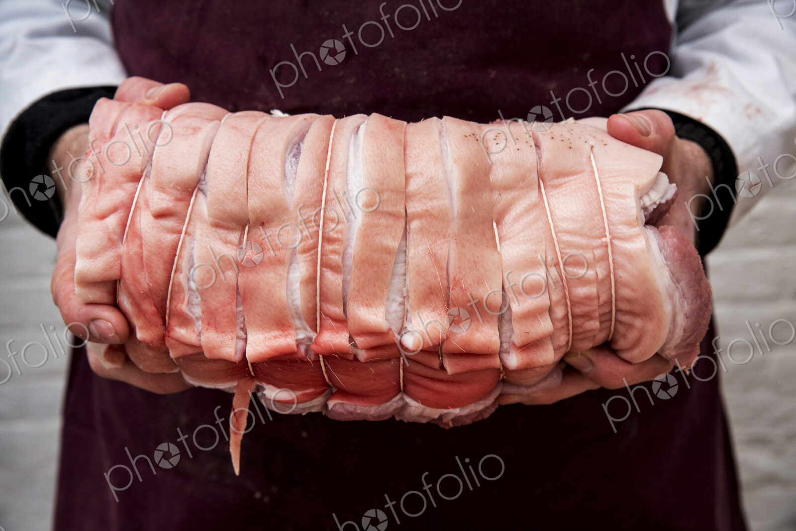 Close up of butcher wearing apron holding large rolled pork belly.