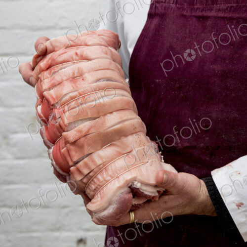 Close up of butcher wearing apron holding large rolled pork belly. Close up of butcher wearing apron holding large rolled pork belly.