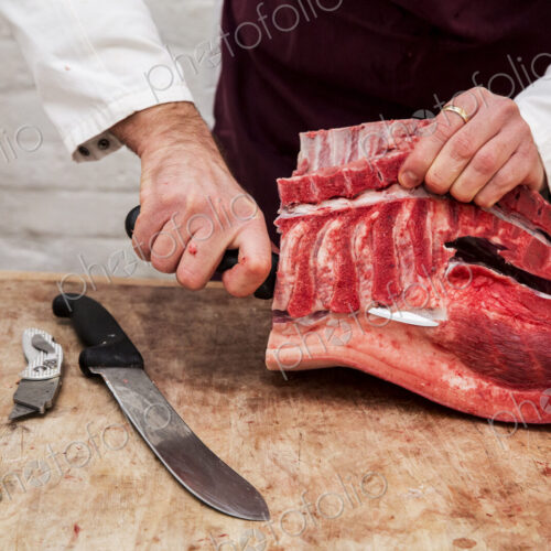 Close up of butcher wearing apron standing at a wooden butcher's block, butchering…