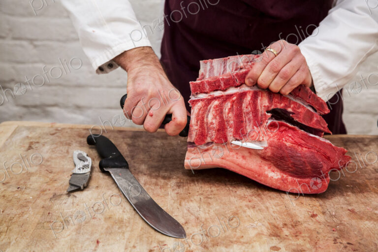 Close up of butcher wearing apron standing at a wooden butcher's block, butchering…