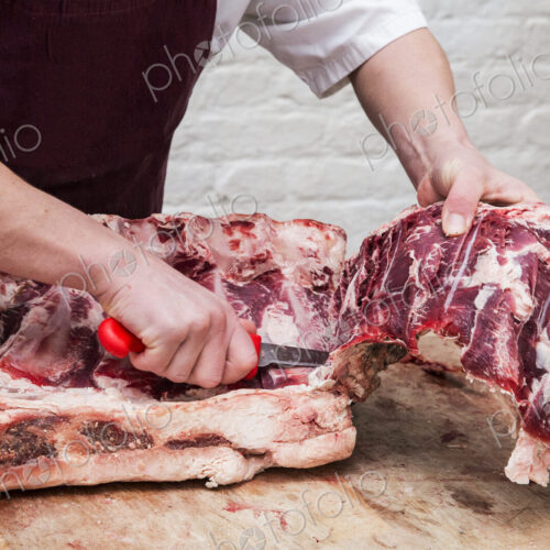 Close up of butcher wearing apron standing at a wooden butcher's block, butchering…