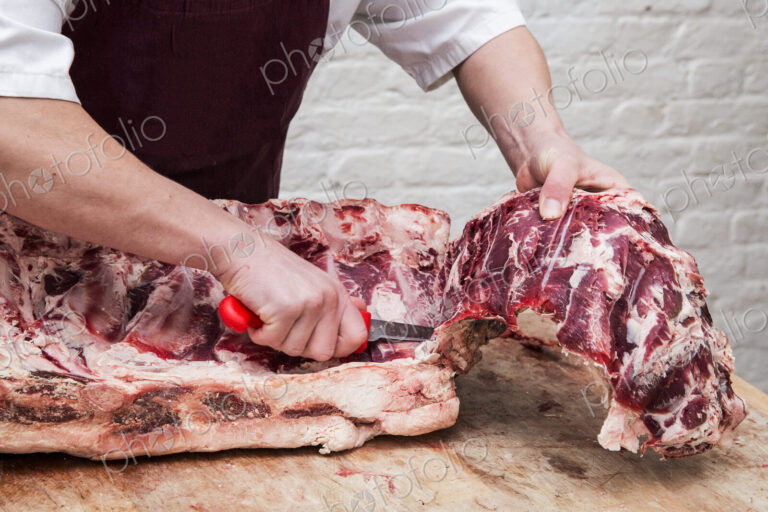 Close up of butcher wearing apron standing at a wooden butcher's block, butchering…