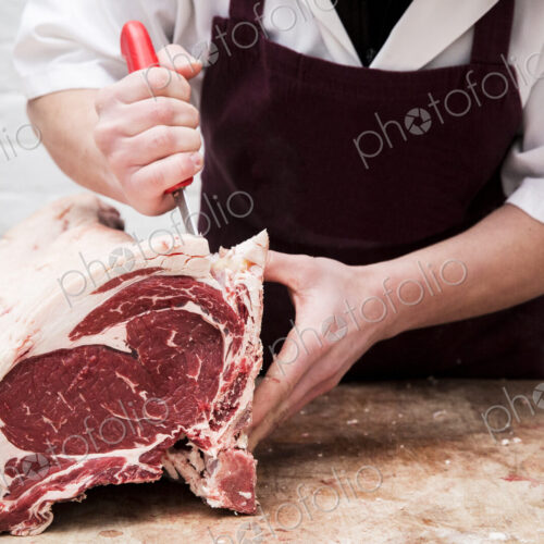 Close up of butcher wearing apron standing at a wooden butcher's block, butchering…