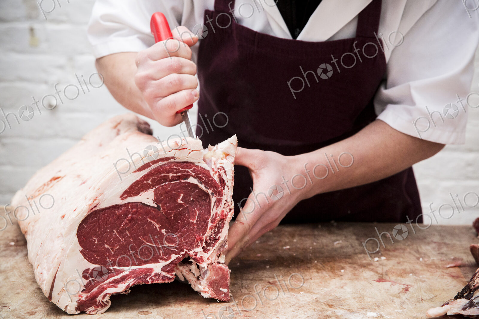 Close up of butcher wearing apron standing at a wooden butcher’s block, butchering…