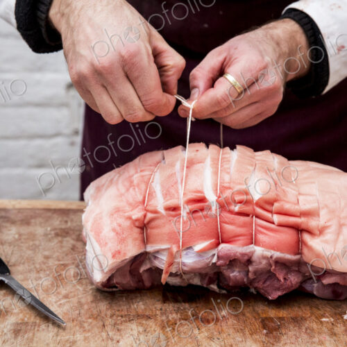 Close up of butcher wearing apron standing at a wooden butcher's block, preparing a…