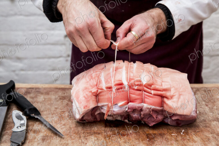 Close up of butcher wearing apron standing at a wooden butcher's block, preparing a…