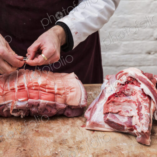 Close up of butcher wearing apron standing at a wooden butcher's block, preparing a…