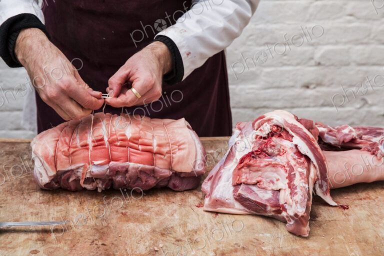Close up of butcher wearing apron standing at a wooden butcher's block, preparing a…
