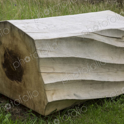 Close up of carved piece of tree trunk with wave pattern lying on grass.